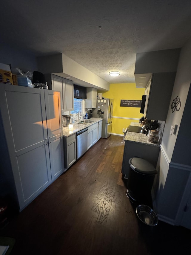 kitchen featuring appliances with stainless steel finishes, sink, light stone countertops, dark wood-type flooring, and a textured ceiling