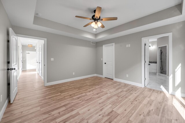 unfurnished bedroom with ceiling fan, connected bathroom, light hardwood / wood-style floors, and a tray ceiling