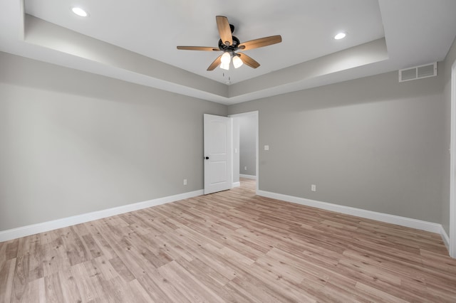 spare room featuring a raised ceiling, ceiling fan, and light hardwood / wood-style flooring