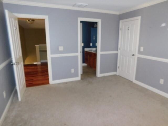 unfurnished bedroom with crown molding, light colored carpet, and ensuite bathroom