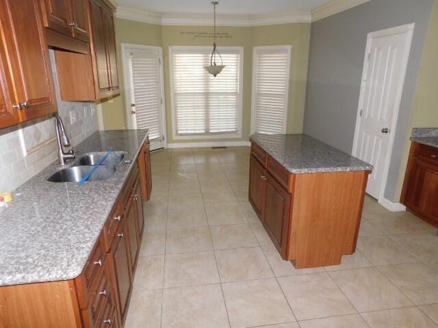 kitchen featuring sink, tasteful backsplash, decorative light fixtures, a center island, and dark stone counters