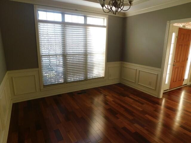 spare room with an inviting chandelier, dark wood-type flooring, and ornamental molding