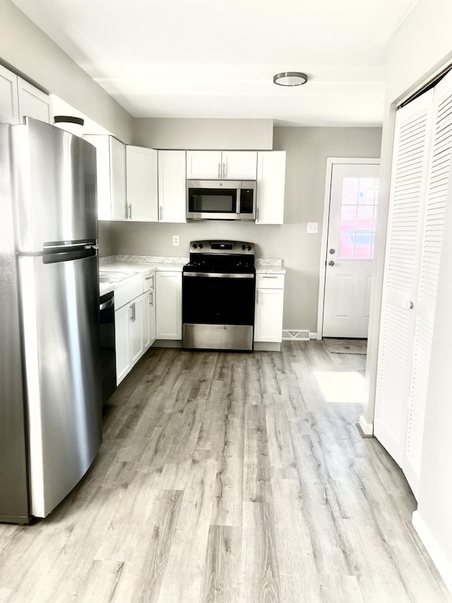 kitchen with stainless steel appliances, white cabinets, and light wood-type flooring