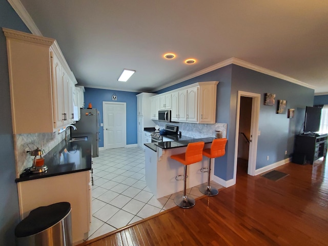 kitchen featuring sink, crown molding, appliances with stainless steel finishes, kitchen peninsula, and light wood-type flooring