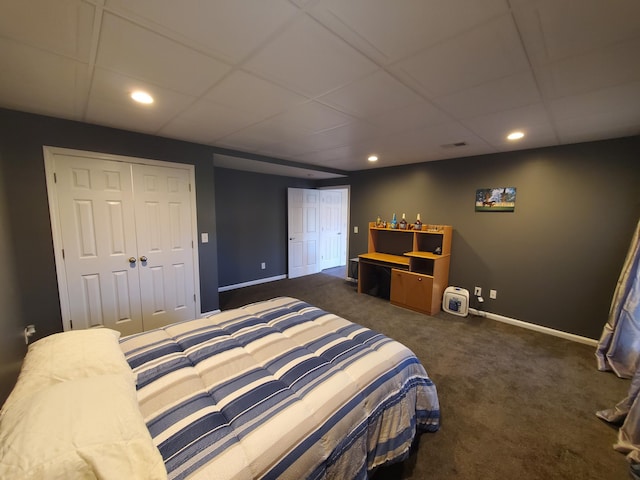 bedroom with a drop ceiling, dark carpet, and a closet