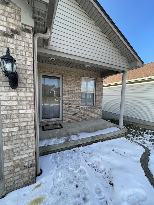 snow covered property entrance featuring brick siding