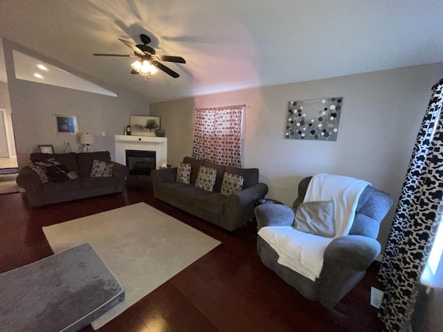 living area featuring lofted ceiling, dark wood-type flooring, a glass covered fireplace, and a ceiling fan