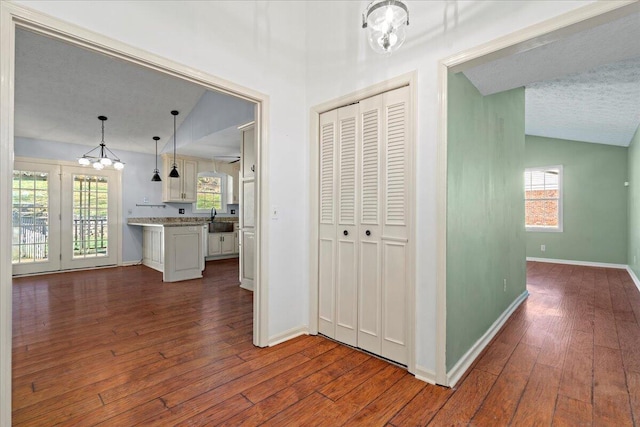 corridor featuring dark wood-type flooring, vaulted ceiling, sink, and a textured ceiling