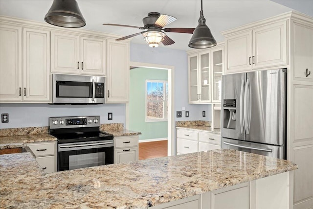 kitchen with stainless steel appliances, ceiling fan, hanging light fixtures, and light stone counters