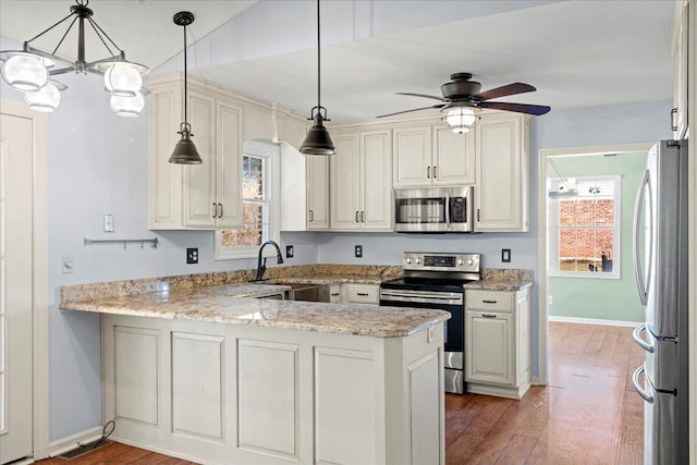 kitchen featuring appliances with stainless steel finishes, pendant lighting, sink, light stone counters, and kitchen peninsula