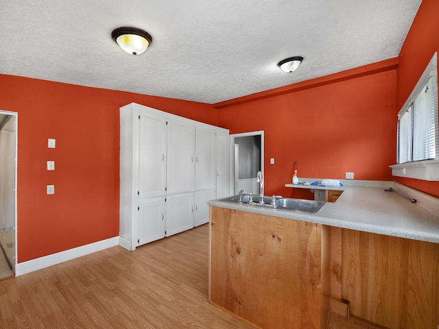 kitchen featuring sink, a textured ceiling, kitchen peninsula, light hardwood / wood-style floors, and white cabinets