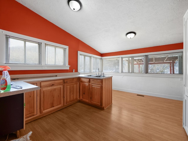 kitchen featuring vaulted ceiling, sink, light hardwood / wood-style floors, kitchen peninsula, and a textured ceiling