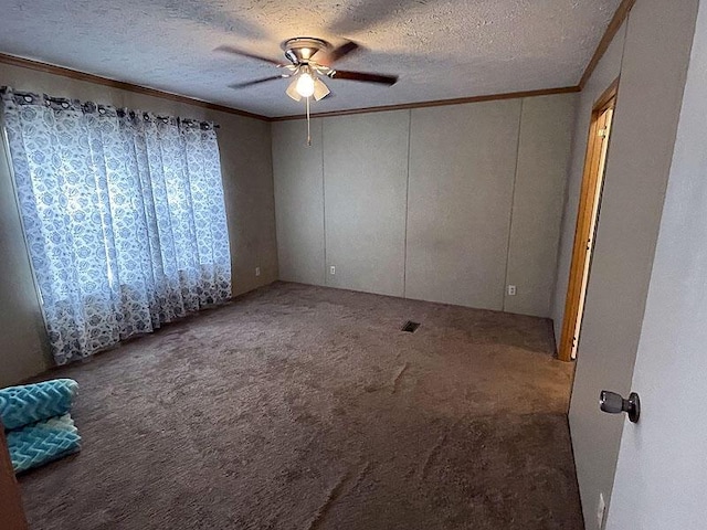empty room featuring ceiling fan, carpet floors, ornamental molding, and a textured ceiling
