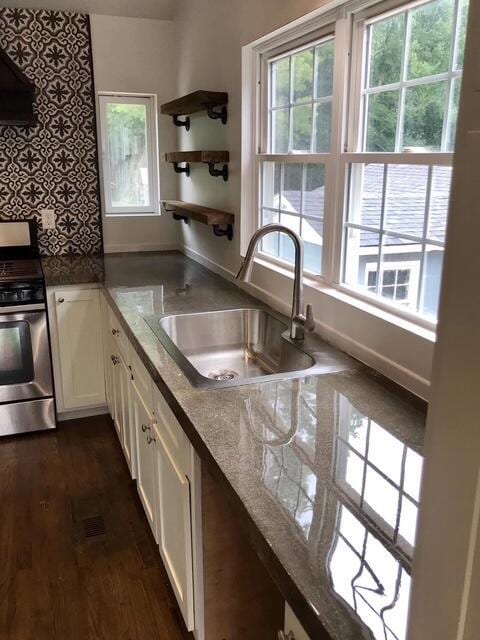 kitchen with a sink, white cabinets, decorative backsplash, dark wood finished floors, and stainless steel range with gas stovetop