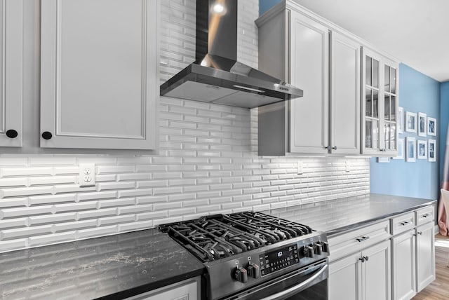 kitchen with wall chimney exhaust hood, stainless steel gas stove, white cabinetry, tasteful backsplash, and light wood-type flooring