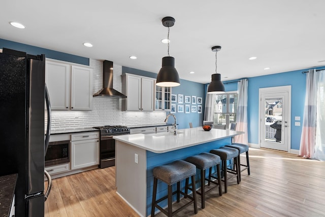 kitchen featuring wall chimney exhaust hood, a breakfast bar, decorative light fixtures, an island with sink, and stainless steel appliances