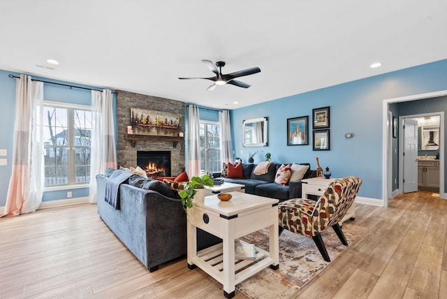 living room featuring ceiling fan, a stone fireplace, and light hardwood / wood-style floors