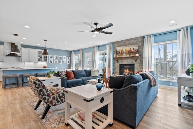 living room featuring sink, a fireplace, light hardwood / wood-style floors, and ceiling fan