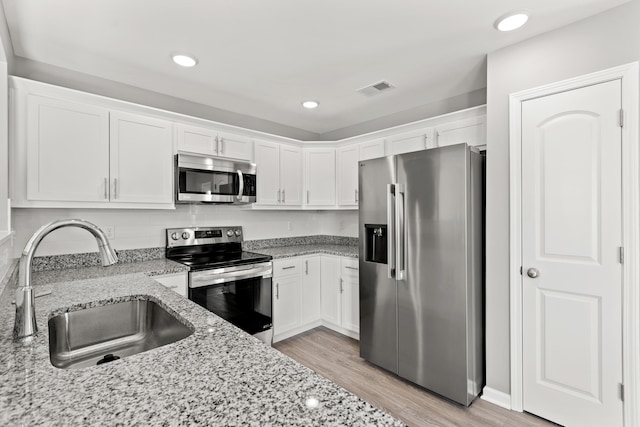 kitchen with sink, light stone counters, light hardwood / wood-style flooring, stainless steel appliances, and white cabinets