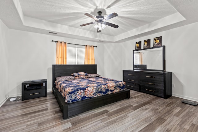 bedroom with ceiling fan, hardwood / wood-style floors, a textured ceiling, and a tray ceiling