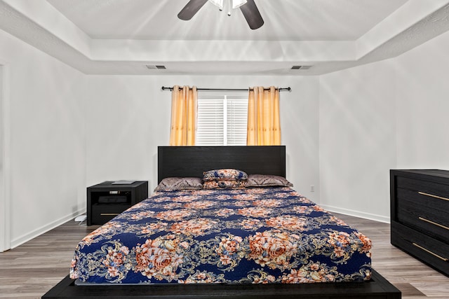 bedroom with ceiling fan, a tray ceiling, and hardwood / wood-style floors