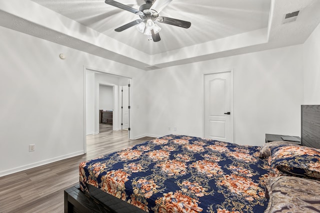 bedroom with ceiling fan, wood-type flooring, and a raised ceiling