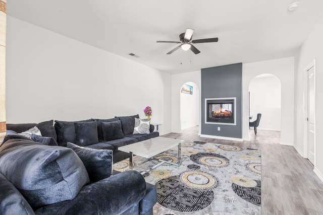 living room featuring ceiling fan, light hardwood / wood-style floors, and a multi sided fireplace