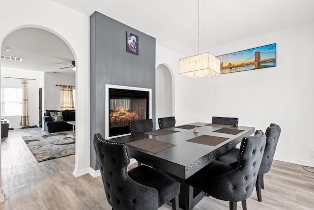 dining room featuring a multi sided fireplace, hardwood / wood-style floors, and ceiling fan