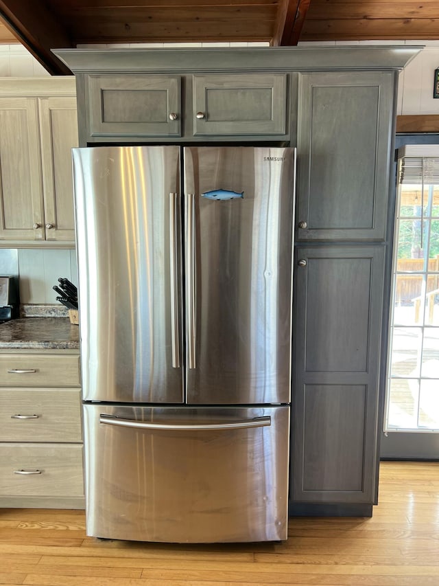 kitchen featuring stainless steel fridge, light hardwood / wood-style floors, dark stone counters, and beamed ceiling