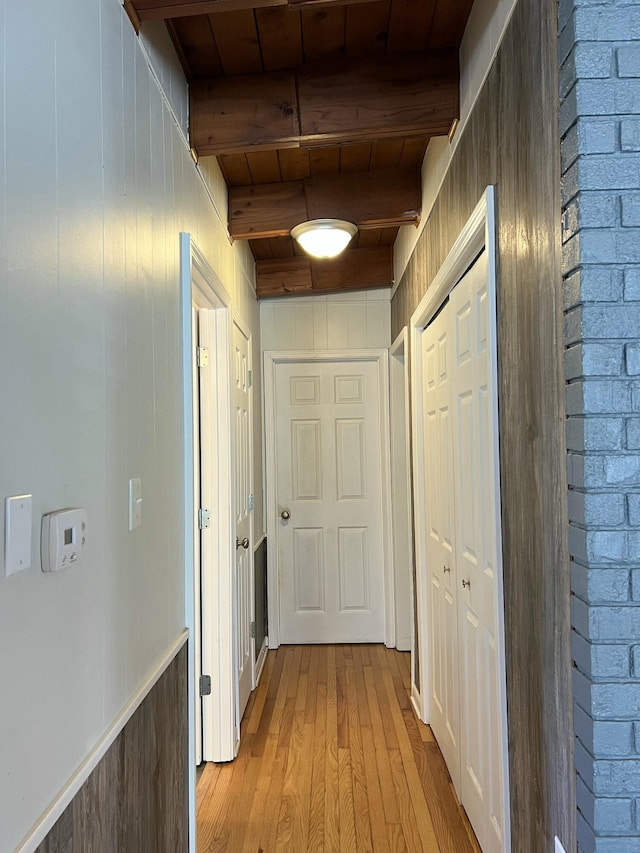 hall featuring wood walls, wooden ceiling, beam ceiling, and light hardwood / wood-style flooring