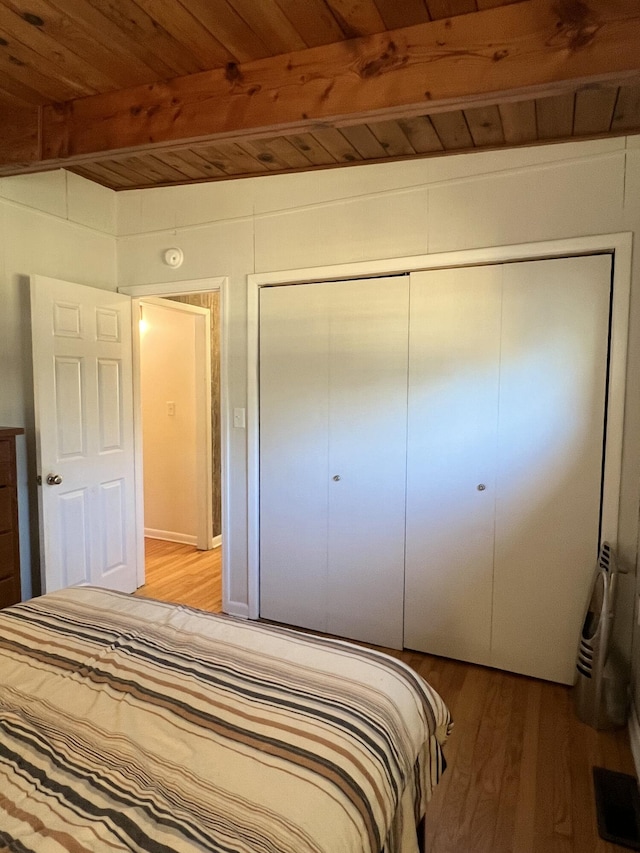 unfurnished bedroom with wood ceiling, beam ceiling, a closet, and light hardwood / wood-style flooring