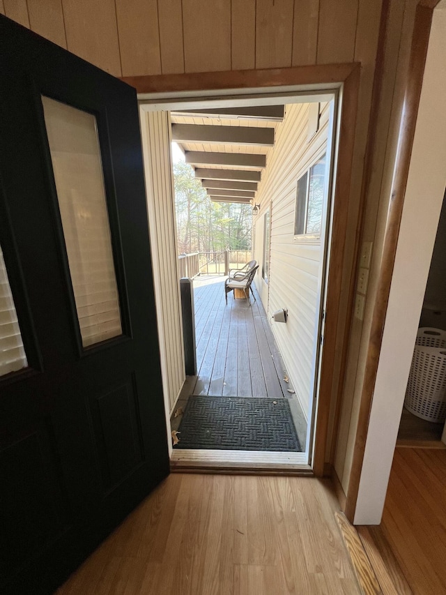 doorway to outside with wooden walls, beam ceiling, and light hardwood / wood-style floors