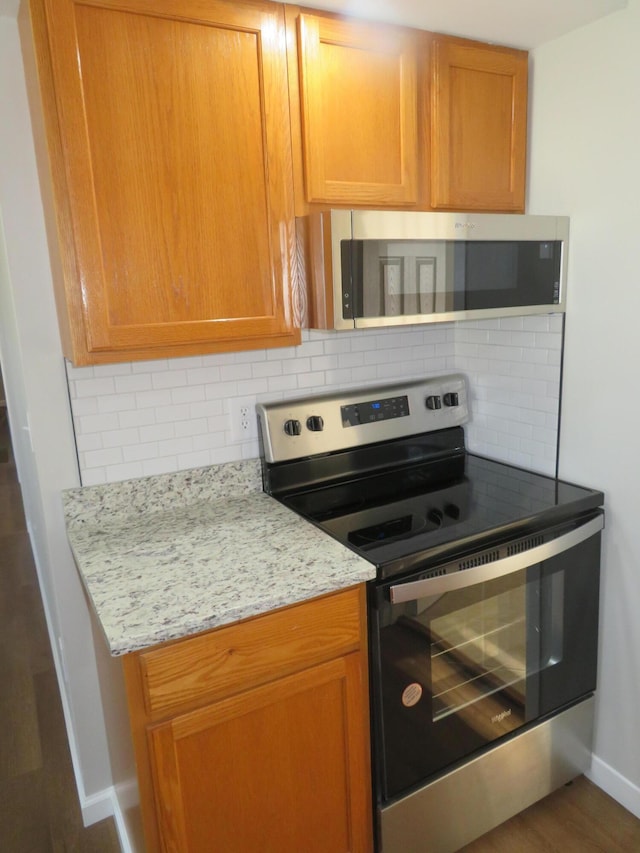 kitchen with dark hardwood / wood-style flooring, decorative backsplash, light stone countertops, and appliances with stainless steel finishes