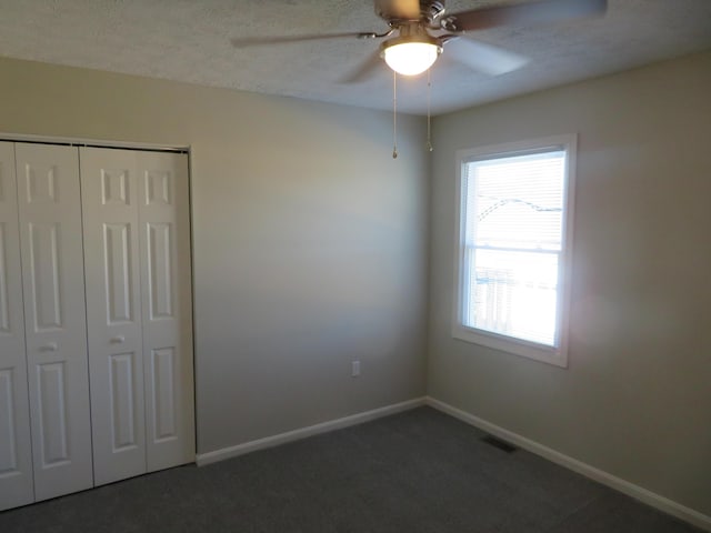 unfurnished bedroom with dark carpet, a textured ceiling, a closet, and ceiling fan