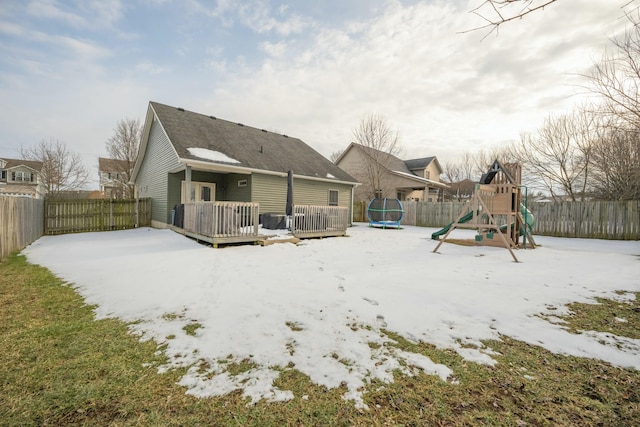 snow covered rear of property with a trampoline, a wooden deck, and a playground