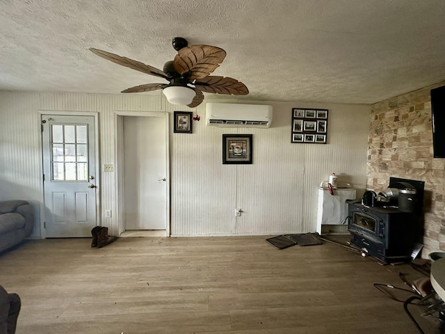 interior space featuring a wood stove, a wall unit AC, ceiling fan, a textured ceiling, and light hardwood / wood-style flooring