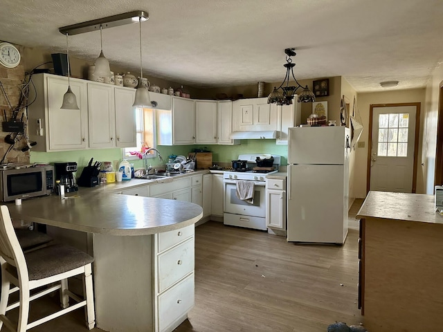 kitchen featuring sink, a breakfast bar area, pendant lighting, white appliances, and white cabinets