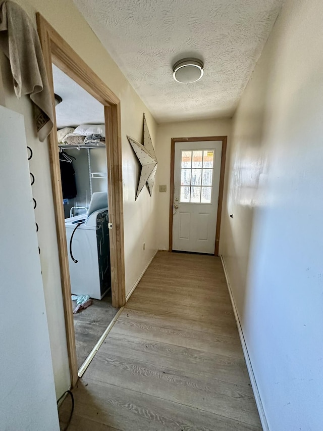 doorway featuring washer / clothes dryer, a textured ceiling, and light hardwood / wood-style floors