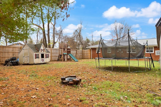 view of yard with a trampoline, a storage shed, a fire pit, and a playground