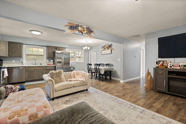 living room featuring a chandelier, sink, a textured ceiling, and light wood-type flooring