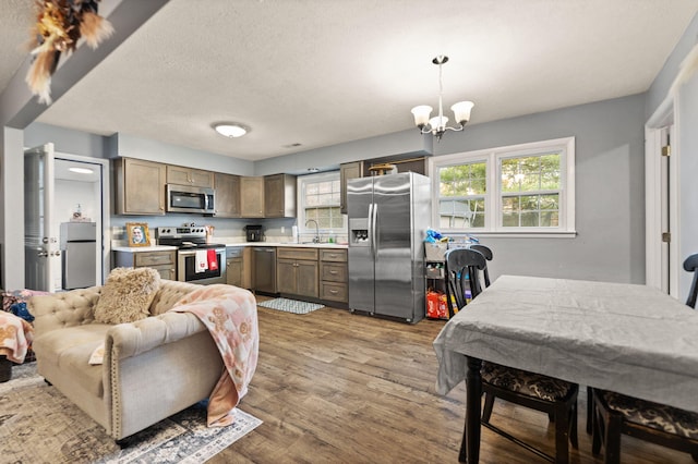 kitchen with sink, appliances with stainless steel finishes, a notable chandelier, wood-type flooring, and decorative light fixtures