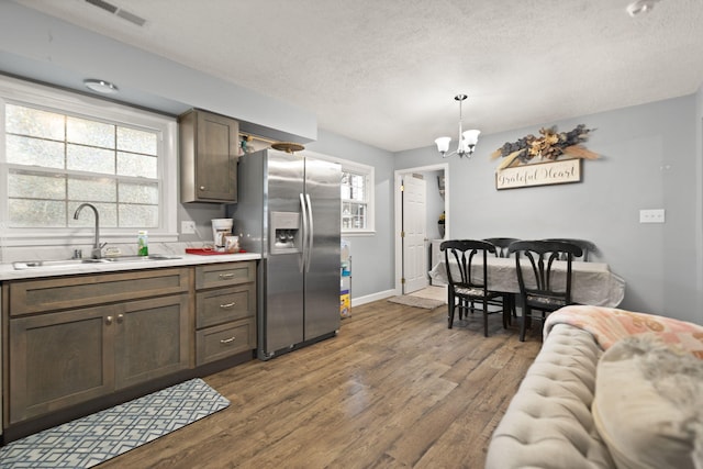 kitchen featuring stainless steel refrigerator with ice dispenser, sink, dark brown cabinets, hanging light fixtures, and dark hardwood / wood-style floors