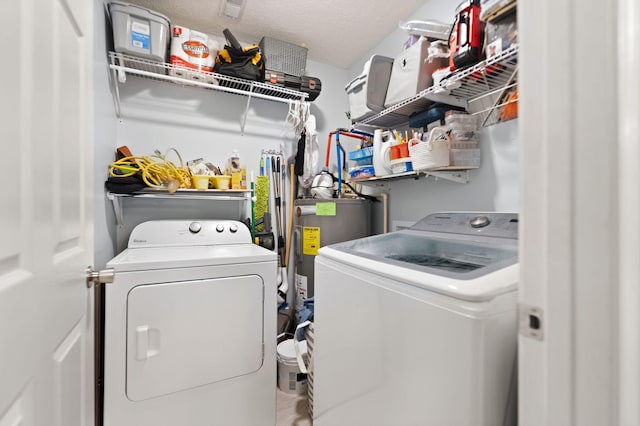 clothes washing area with water heater, a textured ceiling, and washer and clothes dryer