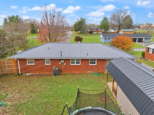 rear view of property featuring a trampoline, central AC, and a lawn