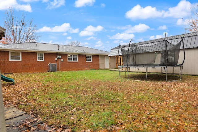 back of house featuring central AC unit, a trampoline, and a lawn