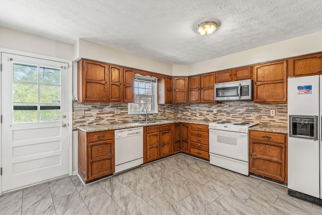 kitchen with tasteful backsplash, light stone countertops, sink, and white appliances