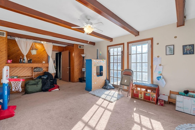 playroom featuring ceiling fan, wooden walls, light colored carpet, and beamed ceiling