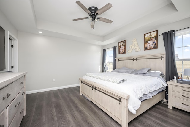 bedroom with dark wood-type flooring, ceiling fan, and a tray ceiling