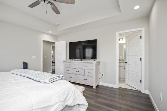 bedroom featuring dark hardwood / wood-style flooring, a tray ceiling, ensuite bath, and ceiling fan