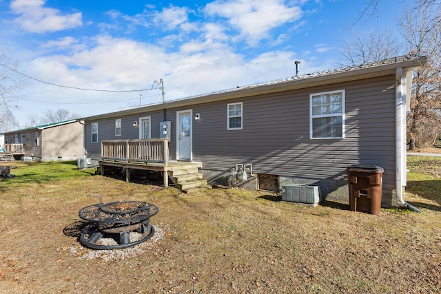 back of property featuring a wooden deck, a lawn, cooling unit, and a fire pit